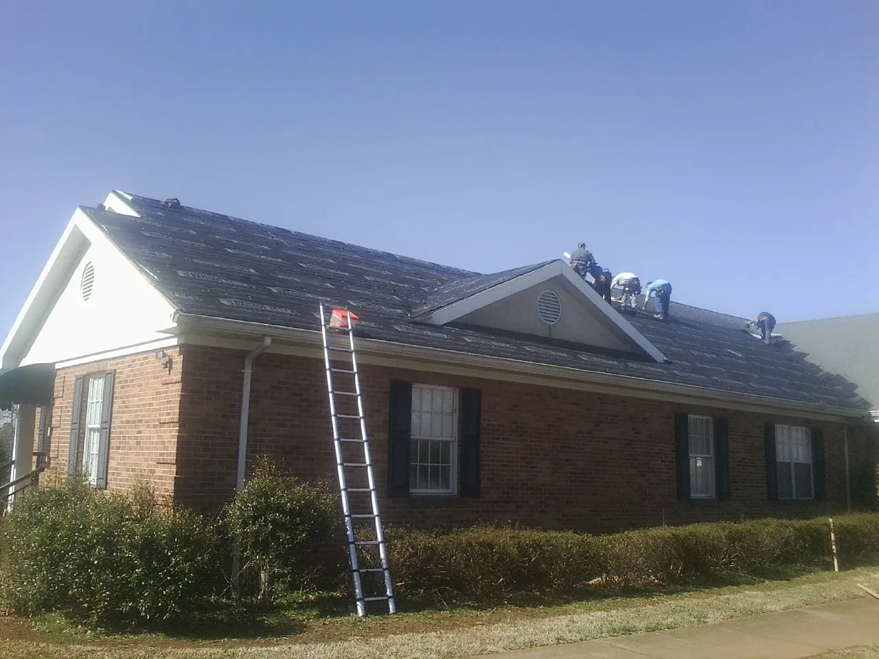 Crew tearing shingles off a brick ranch roof with a ladder set — Metal Roof Repair work by our crew in Merced