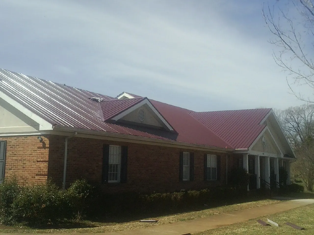 Red metal roof with gabled entries on a long brick building, from a Hail Damage Roof Repair job in Merced