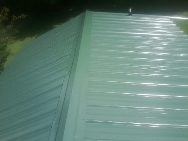 New green metal panels meeting at the ridge of a roof — Flat Roof Repair work by our crew in Merced