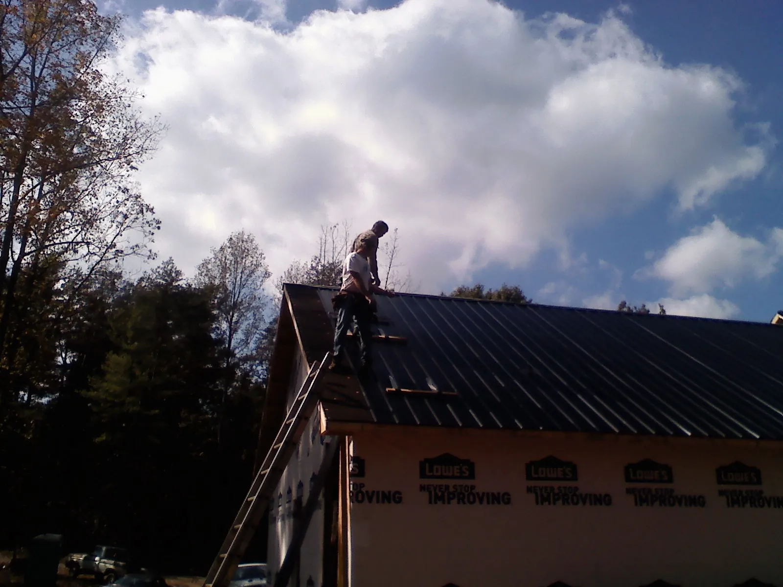 Roofer fastening dark metal panels high against a cloudy sky, from a Roof Inspection job in Merced