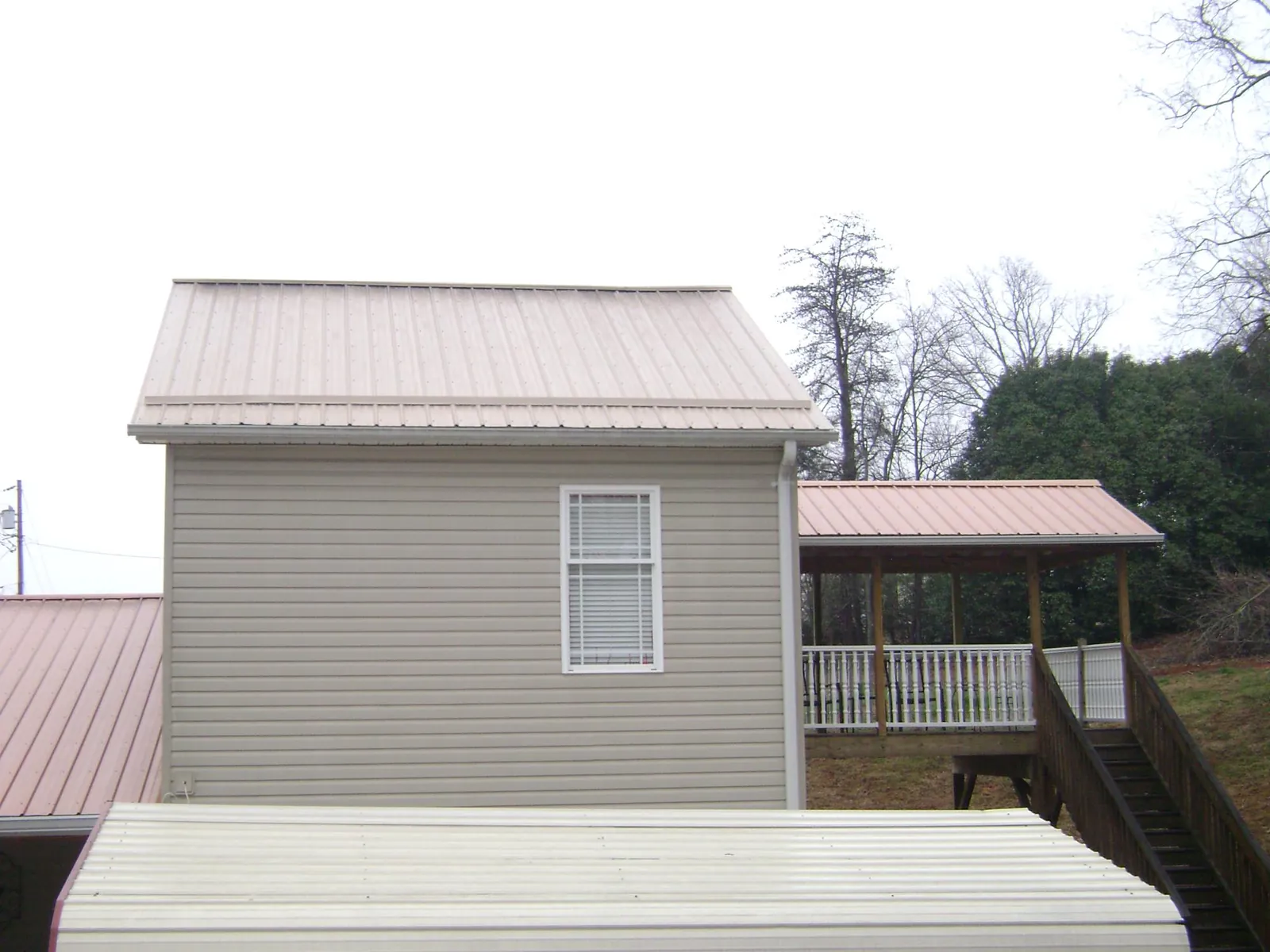 Tan metal roofs on a two story addition and attached porch, from a Roof Replacement job in Merced